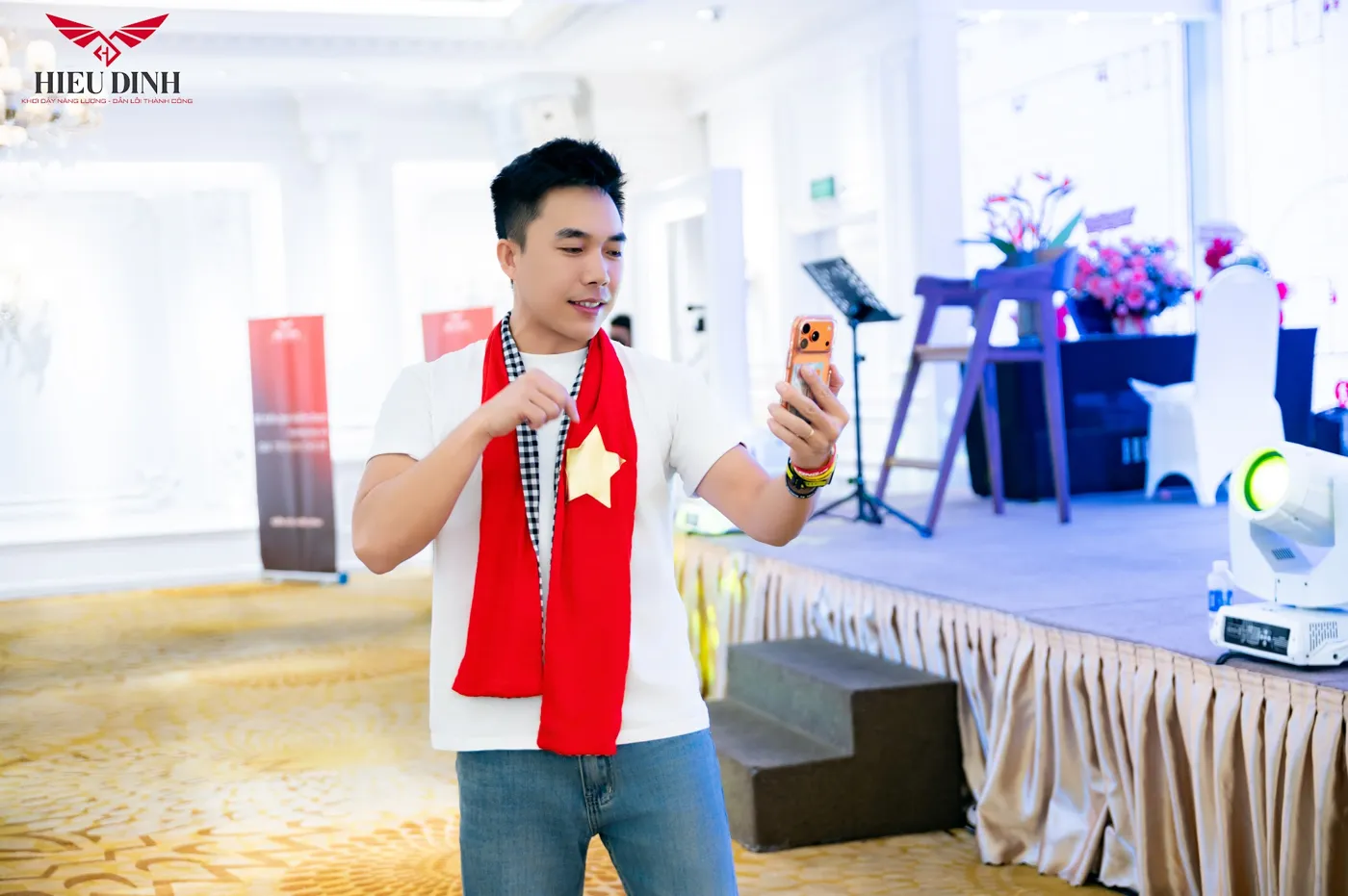 Thầy Hiếu cười nói trên sân khấu, khăn đỏ quàng cổ